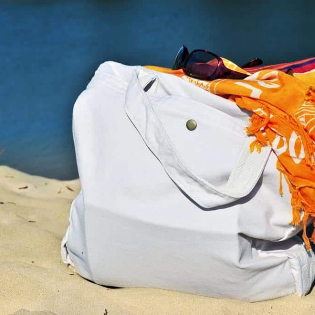 Summer beach bag on sand with towels and sunglasses